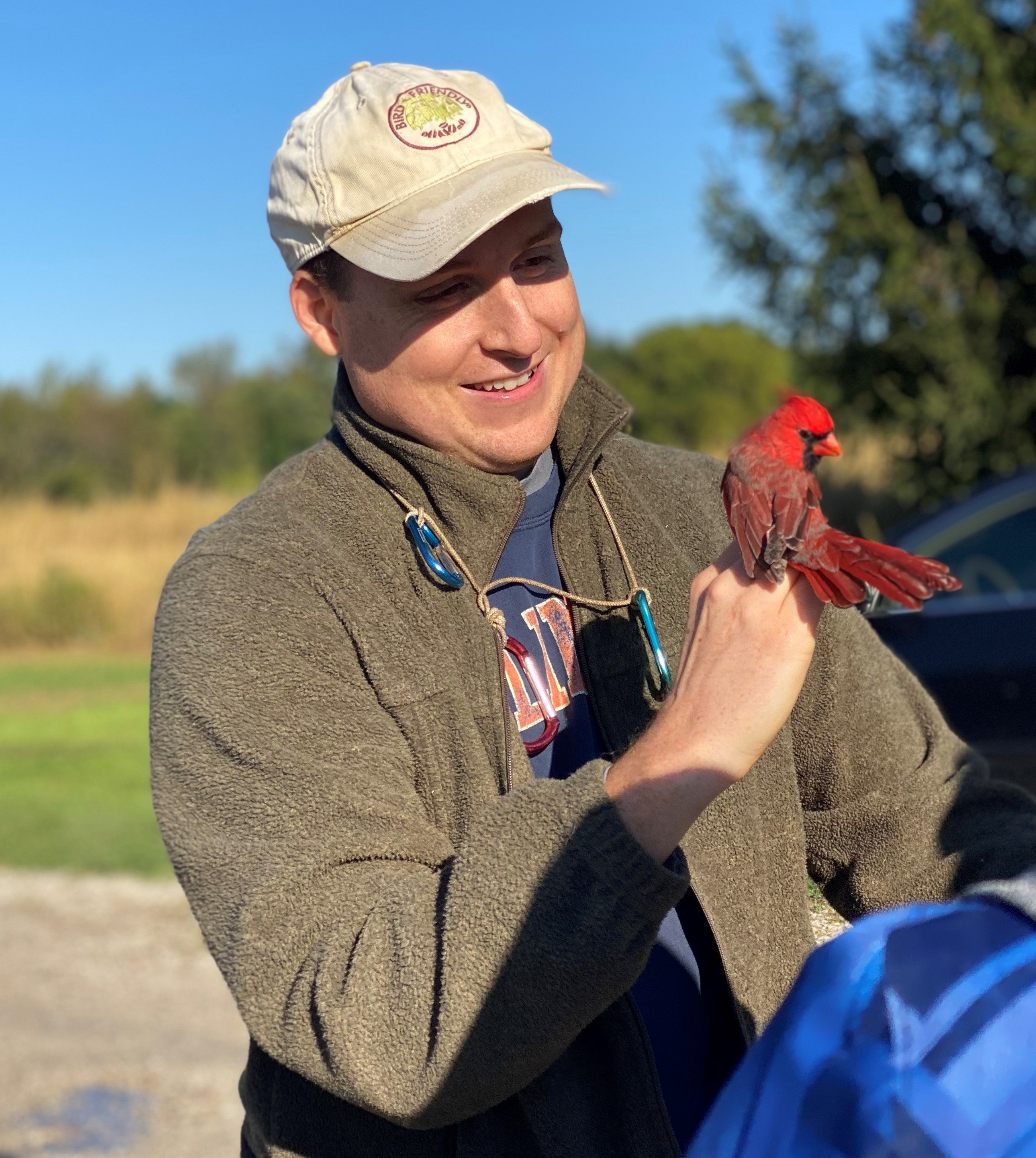 Photo of Todd Jones holding a northern cardinal and smiling. The cardinal is a bright red bird. 
