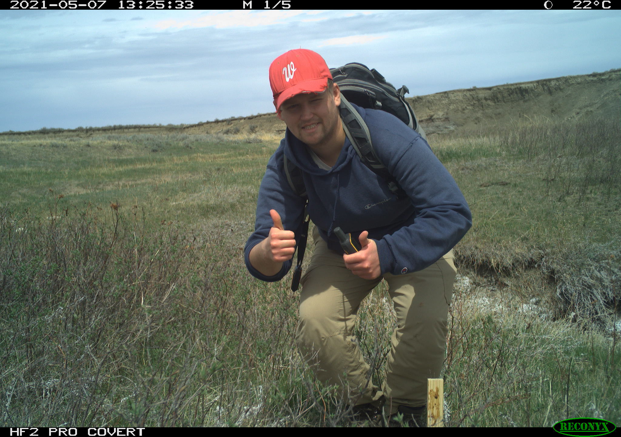 Photo of Johnny Stutzman flashing a thumbs up at the camera. Beside him is a wooden stake which he has covered with a scent lure.