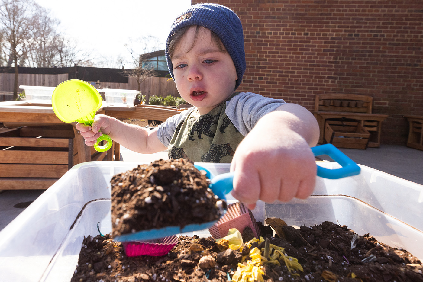 A toddler scoops dirt in a tub with a small plastic shovel.