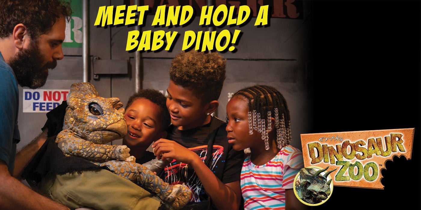 Three children interact with a baby dinosaur puppet while the puppeteer looks on