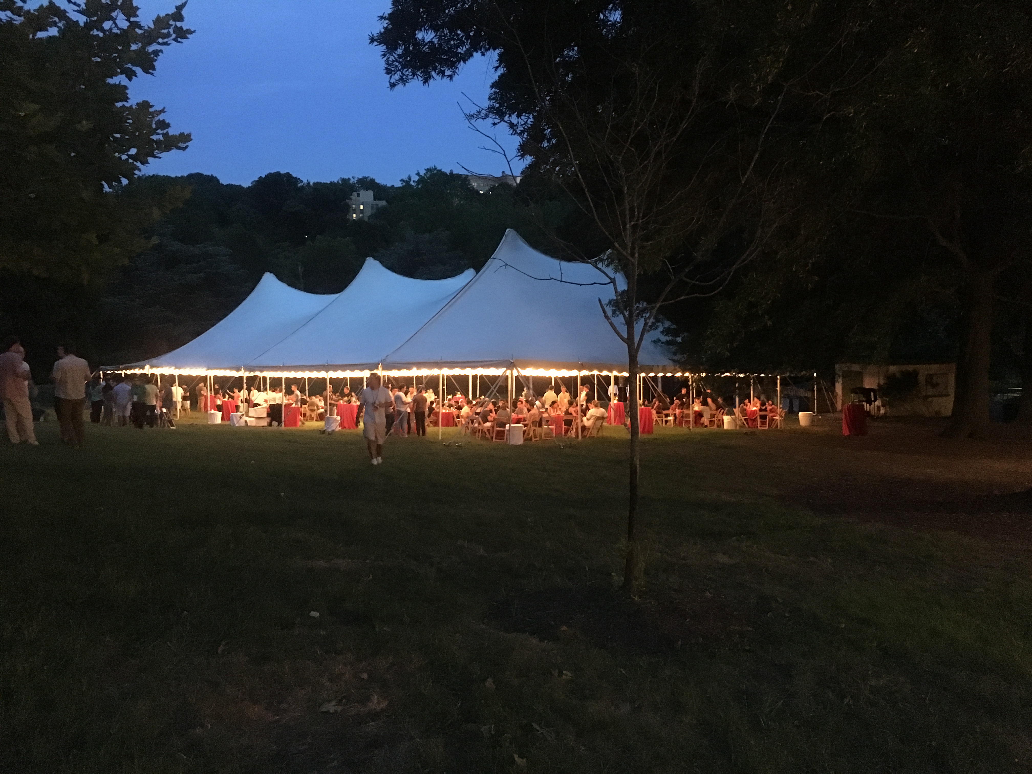 A large event tent set up with table and lights in the evening in a grassy field