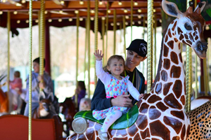 man with a child riding the Speedwell Foundation Conservation Carousel