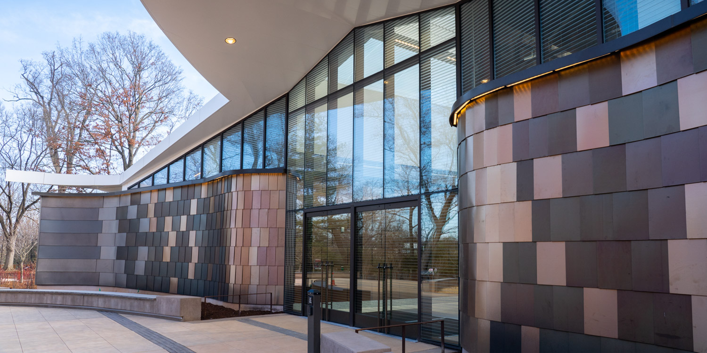 Exterior of the Bird House. The entryway is made of transparent glass with barely-visible line patterns on the glass. The entrance was inspired by the slate gray and rusty brown plumage of the sandhill crane, a species that visitors can see outside.