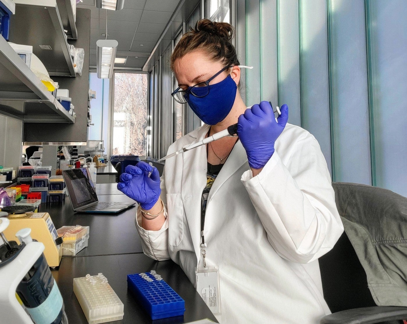Scientist at a lab bench using a long pipette and holding a small tube in her other hand