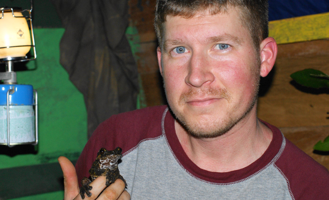Matt Evans looks at the camera holding a brown tree frog in Panama. He is indoors.