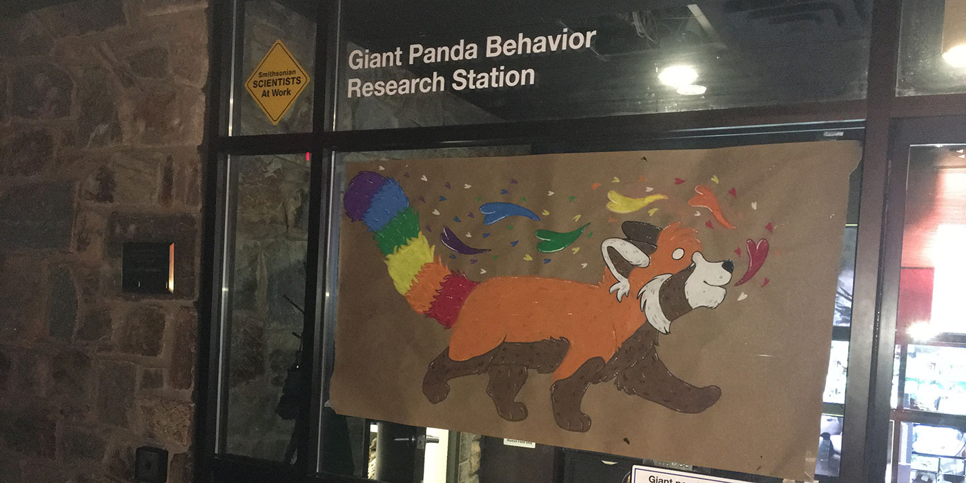A painted sign of a red panda with a rainbow-colored tail