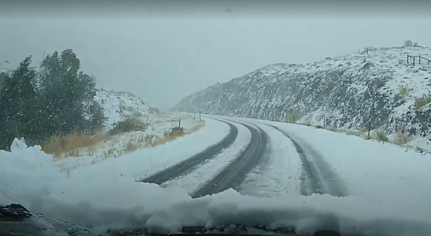 A snow-covered road in Wyoming with trees to the left and hills to the right.