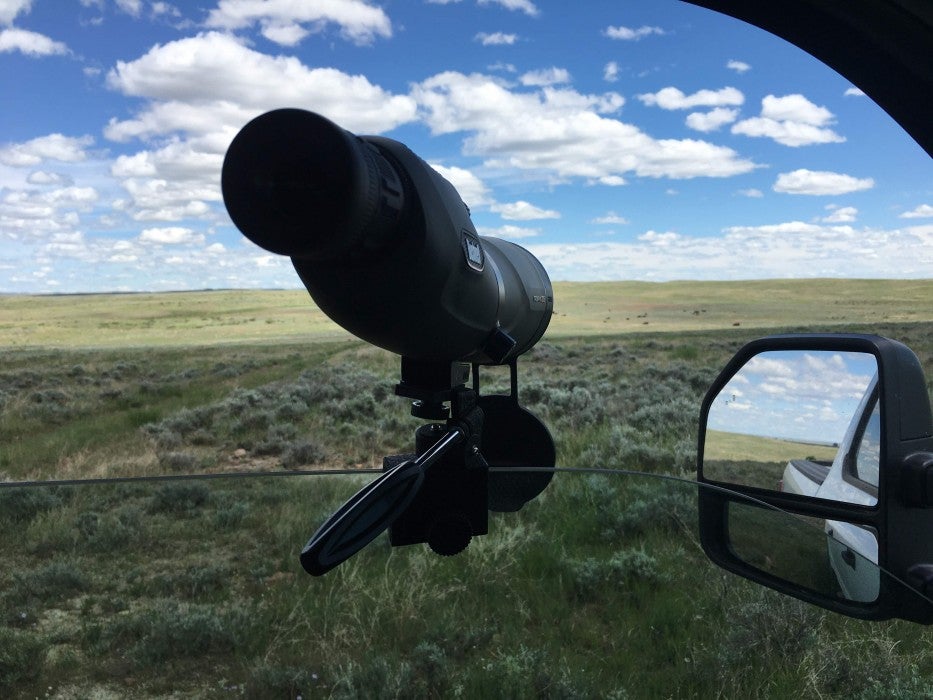 A spotting scope attached to a partially rolled down car window allows researchers to look out across the prairie and observe bison from their vehicles.