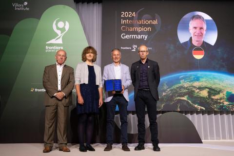 A woman and three men stand on a stage to accept an award. In the background, text on a screen reads, "2024 International Champion: Germany"