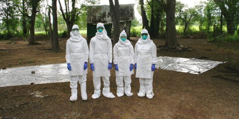 four researchers wearing coveralls and masks standing in a forest