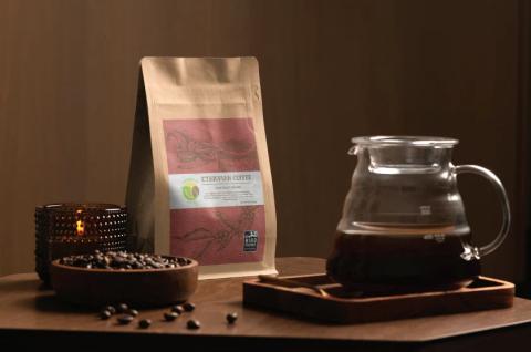 a coffee bag on a wooden surface with coffee beans, a candle, and a pour over pitcher containing coffee surrounding it