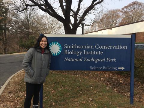 An intern with the Smithsonian Migratory Bird Center poses for a photo next to the sign for the Smithsonian Conservation Biology Institute's Science Building