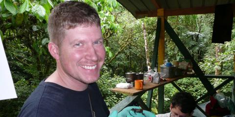 Matt Evans holds a brown tree frog in an outdoor workspace in Panama.