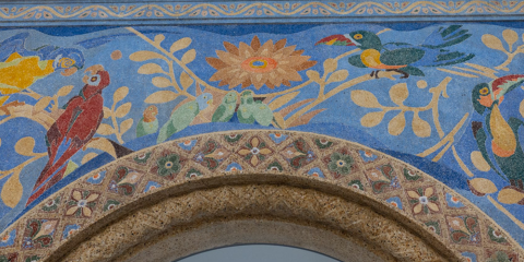 A close-up of colorful birds, including two parrots and two toucans, depicted on the historic arch at the center of the Bird House's lobby..