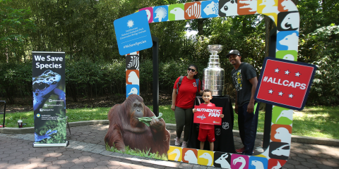 two adults and a young boy pose in front of the Stanley Cup on display at the Zoo