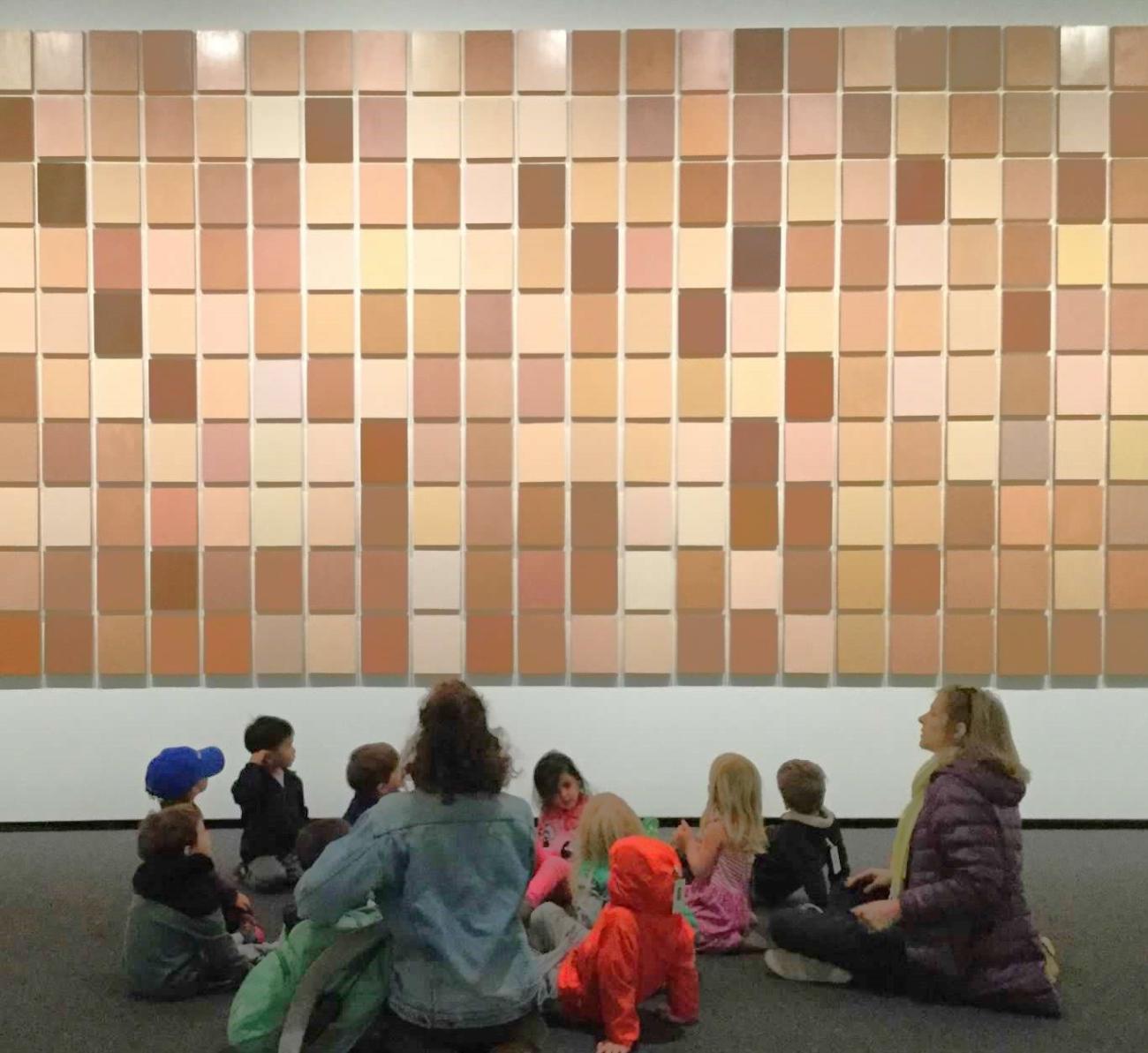 Children look up at an art installation of squares in different shades of flesh tones