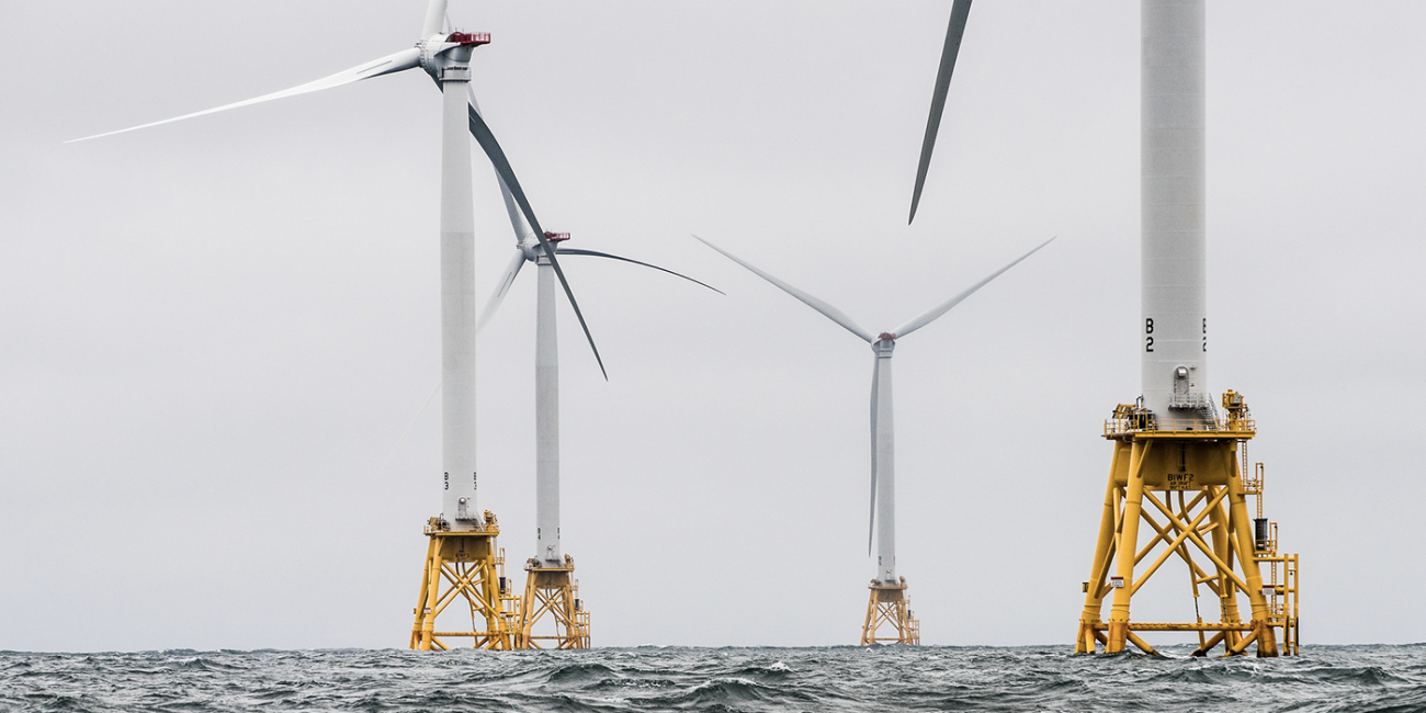 A group of massive wind turbines rising out of the sea.