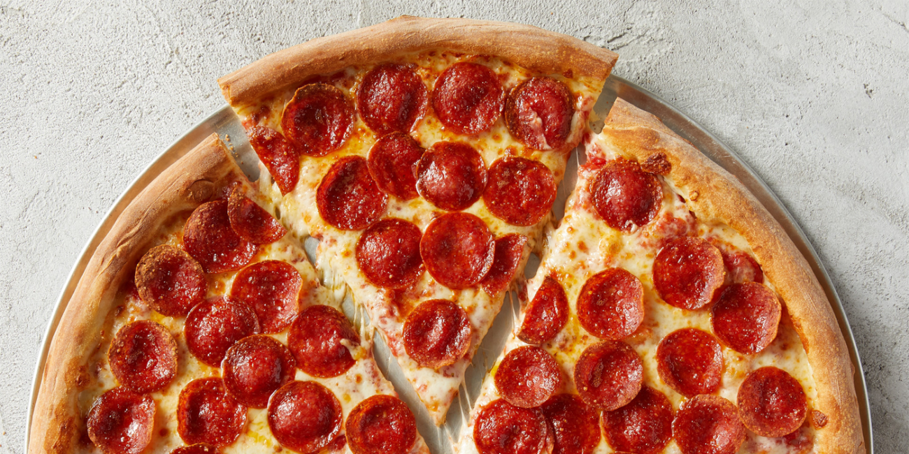 A half-pie of pepperoni pizza with a slice gently pulling apart in the middle.