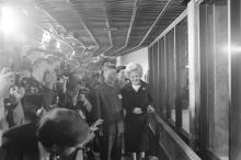 Journalists stand in a crowd and photograph giant pandas; First Lady Patricia Nixon stands in front of them outside the indoor giant panda habitat