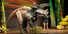 A woman stands on stage next to a large dinosaur puppet