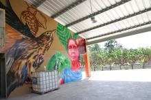 Colorful mural featuring brown spotted bird and woman along with cacao pods and green leaves.
