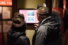 Two visitors wearing paper panda hats interact with a touchscreen exhibit in the Panda House during the Smithsonian's National Zoo's Giant Panda Housewarming Celebration