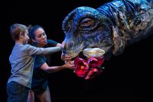 During an "Erth's dinos zoo live" performance, a cast member and child put flowers in the mouth of a larger-than-life dinosaur puppet