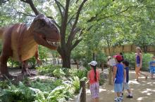 Visitors to a Zoo or theme park look at a large, animatronic T. rex dinosaur