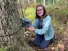 A female scientist posing next to a camera trap tied to a tree