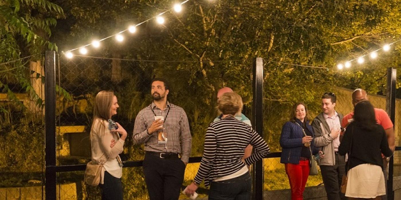 A group of people talking and enjoying drinks under lights outside the Great Cats exhibit in the evening at the Smithsonian's National Zoo