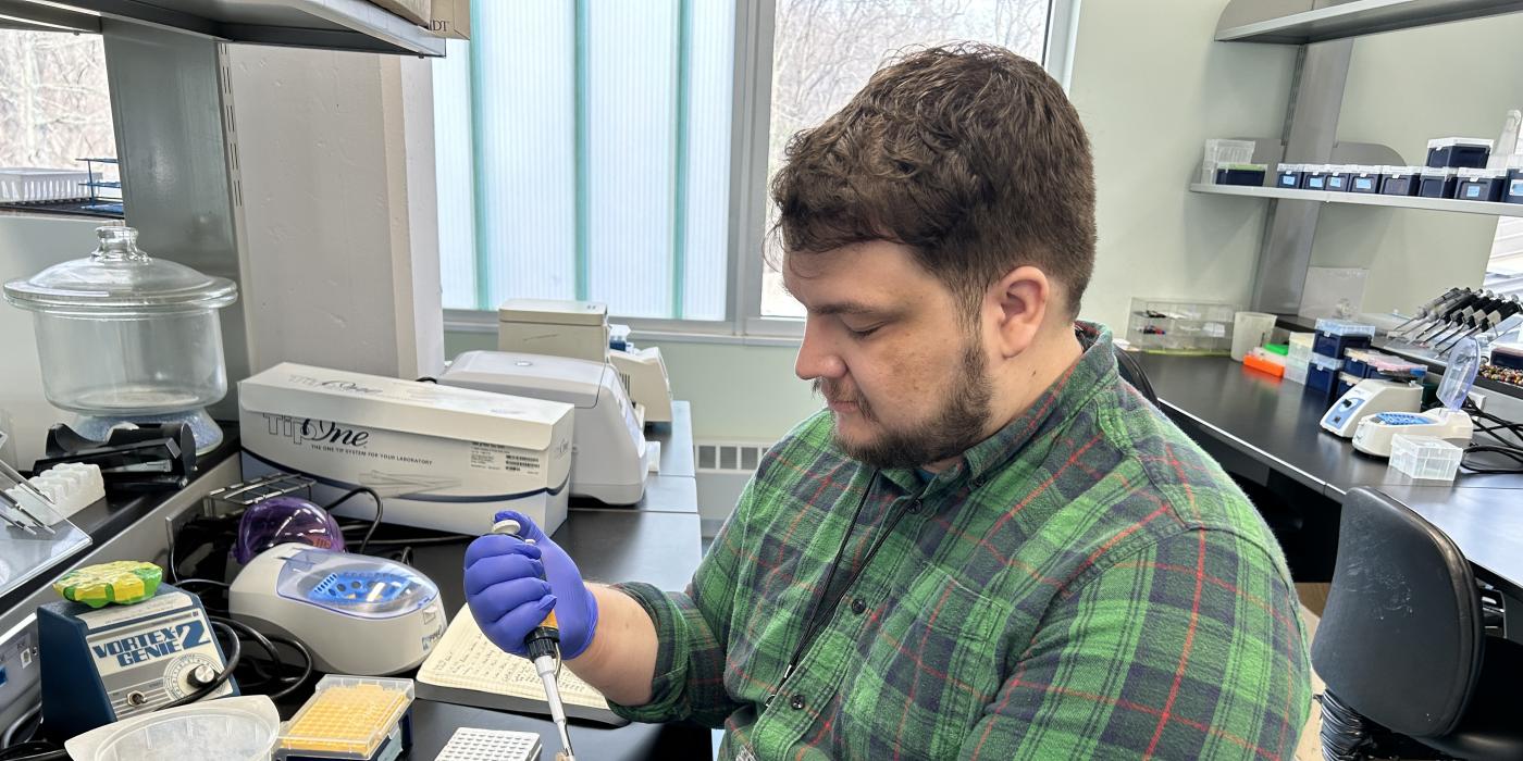 A photo of Sean Lyons in a lab setting. He is using a pipette to put fluid into a small vial. 