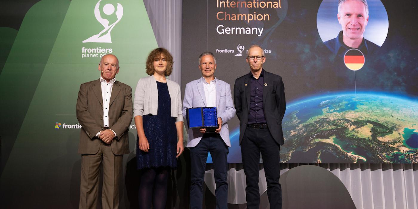 Frontiers Planet Prize Award A woman and three men stand on a stage to accept an award. In the background, text on a screen reads, "2024 International Champion: Germany"