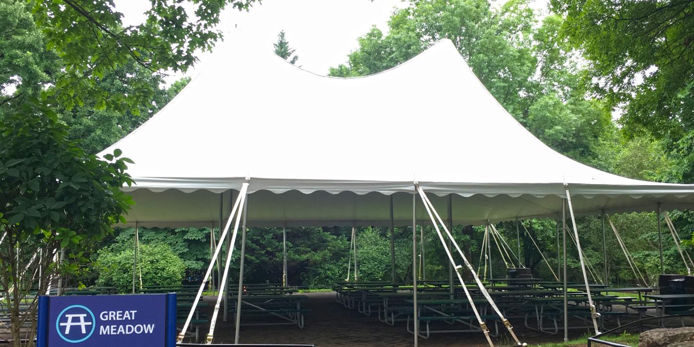 A large event tent set up over a brick path surrounded by trees at the Smithsonian's National Zoo's Great Meadow