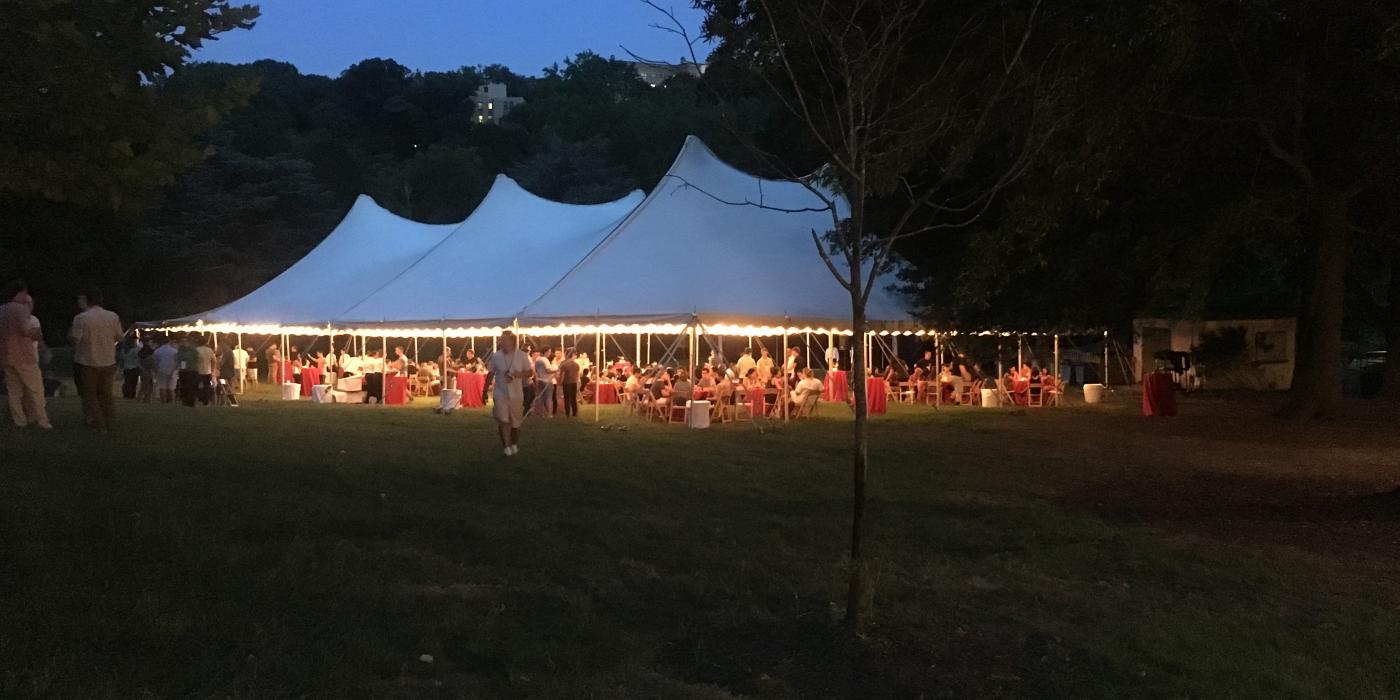A large event tent set up with table and lights in the evening in a grassy field