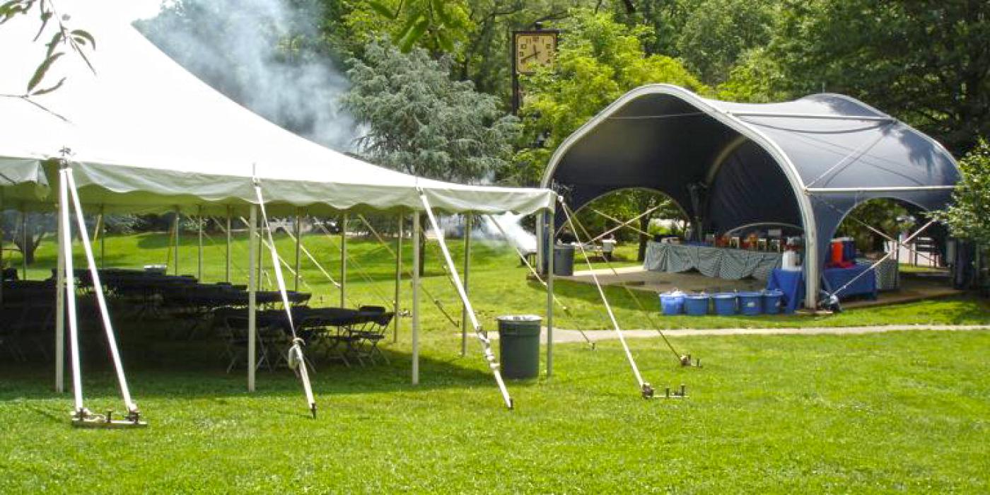 An event tent, tables and chairs set up in a grassy green meadow surrounded by trees on a sunny day at the Smithsonian's National Zoo