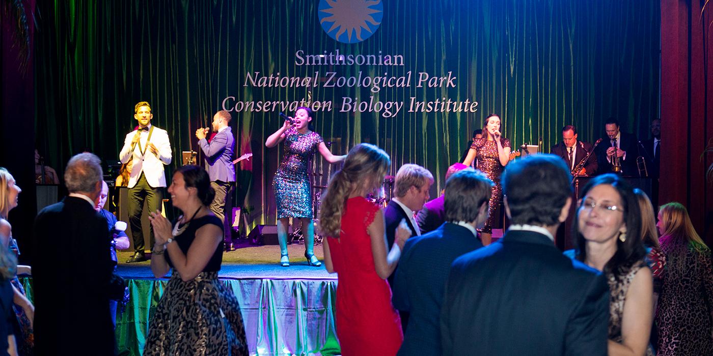 A group of guests with a band playing on stage in the background at the Smithsonian's National Zoo's Monkey Business Gala