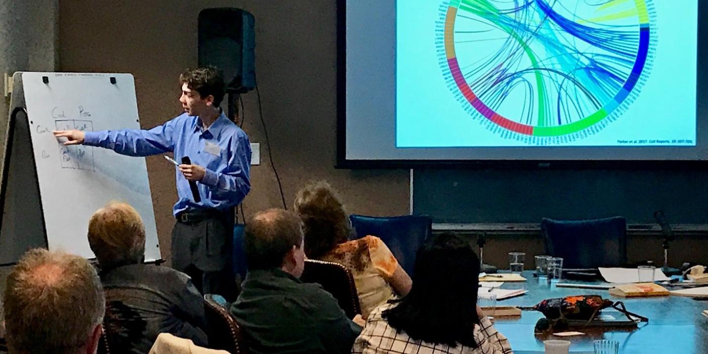 A man points at an easel during a presentation to a small group of people.