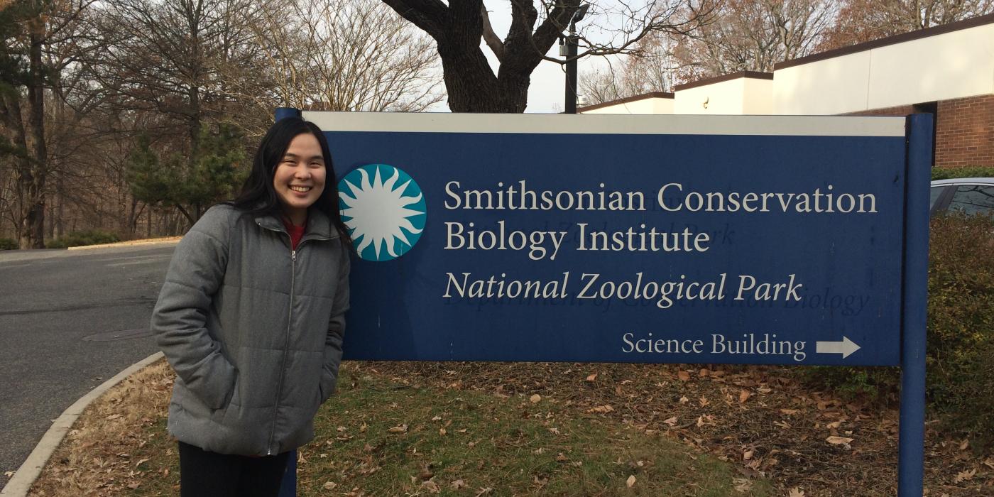 An intern with the Smithsonian Migratory Bird Center poses for a photo next to the sign for the Smithsonian Conservation Biology Institute's Science Building