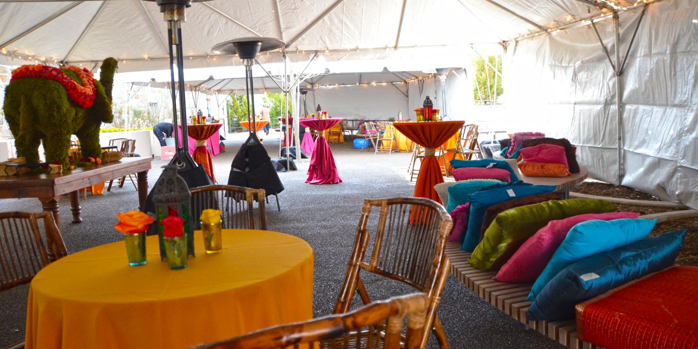 这是一场丰富多彩的宴会，设于一个大帐篷下，配有鸡尾酒桌、带枕头和灯的长椅